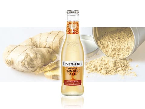 Bottle of Fever-Tree Premium Ginger Ale, a British premium mixer, in front of fresh ginger root and ginger powder