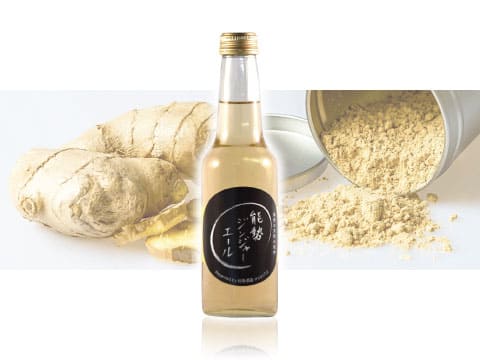 Clear glass bottle of Nose Ginger Ale, a craft ginger ale made by an Osaka sake brewery, in front of fresh ginger root and ginger powder