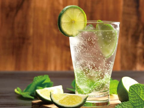 Sparkling gin and tonic in a tall glass with a lime wheel, fresh mint and lime wedges on a wooden table