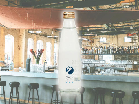 Bottle of n.e.o Premium Tonic Water, a Japanese tonic made with Okinawan shikuwasa, in front of a bright bar counter