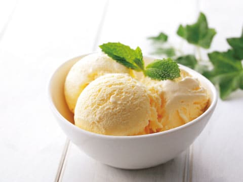 Three scoops of creamy vanilla ice cream topped with a fresh mint sprig in a white bowl on a white wooden table, a dessert pairing for cream cocktails