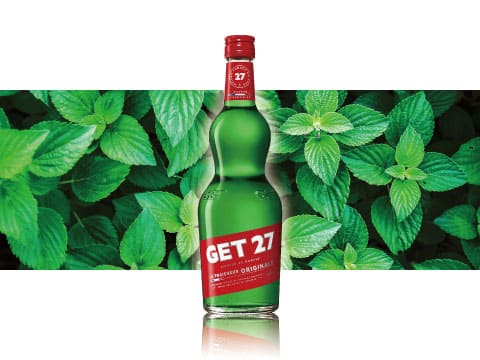 Bottle of GET 27 green peppermint liqueur in front of a backdrop of fresh mint leaves