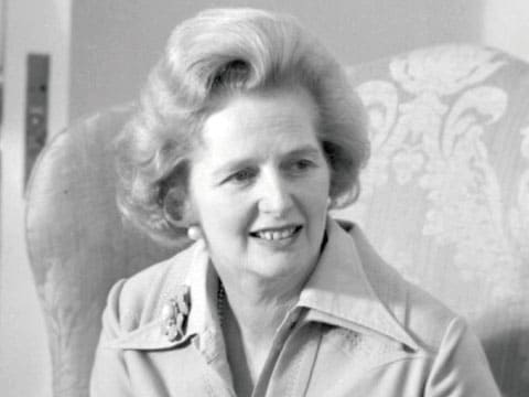 Black-and-white portrait of former British Prime Minister Margaret Thatcher, known as the "Iron Lady," smiling while seated in an armchair