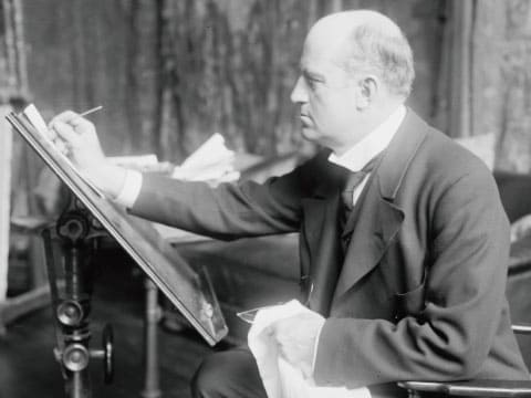Black-and-white photograph of illustrator Charles Dana Gibson, creator of the Gibson Girl, drawing at a tilted easel in his studio, the man most often linked to the Gibson cocktail's name