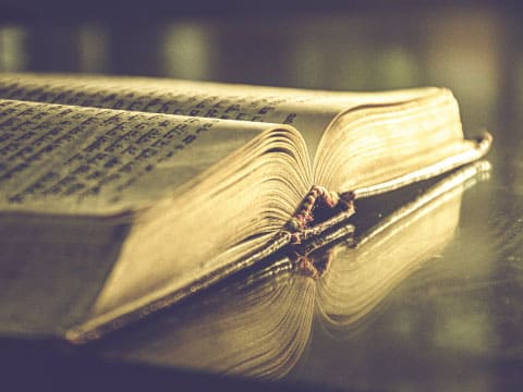 Close-up of an open antique book with worn pages and a ribbon bookmark in warm sepia tones