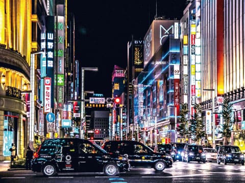 Ginza's main street in Tokyo at night, lined with glowing neon signs and luxury shops, with black taxis waiting at a crossing — the district that gives the Ginza Street cocktail its name