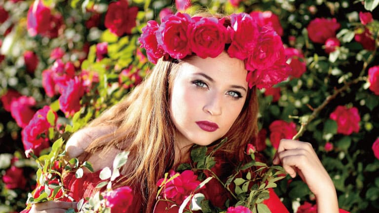 Young woman wearing a crown of red roses, surrounded by blooming red rose bushes in a garden