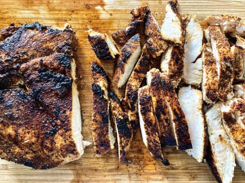 Spice-rubbed grilled chicken breast with a dark, charred crust, partly sliced on a wooden cutting board to show its juicy white interior, a jerk-style pairing for the Caribbean Iceberg cocktail