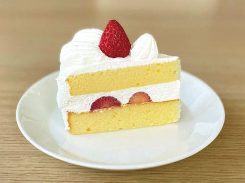 A slice of Japanese-style strawberry shortcake with light sponge layers, whipped cream and fresh strawberries on a white plate, a creamy dessert pairing for the Alice mocktail