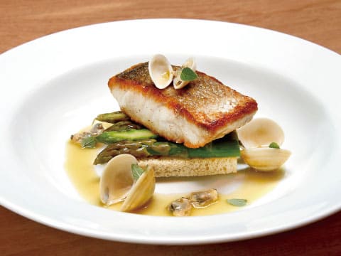 Pan-seared white fish fillet with crispy golden skin, served with clams and asparagus in a light butter sauce, a bright food pairing for a Cognac Orange cocktail