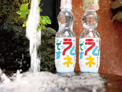 Two classic Japanese ramune soda bottles chilling in fresh running water beside mossy rocks
