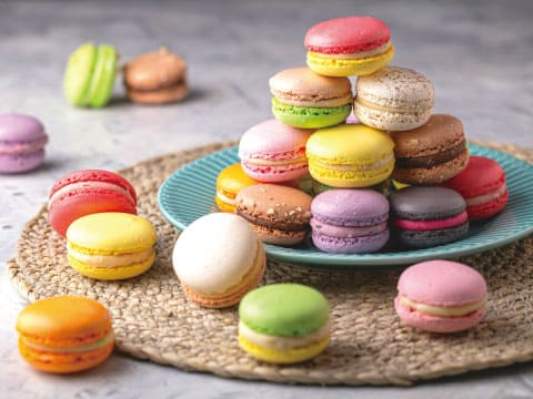 Colorful French macarons stacked on a teal plate and scattered across a woven placemat on a light gray table