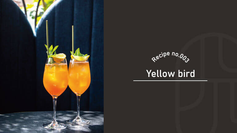 Two orange Yellow Bird cocktails in flute-style glasses, garnished with lime wheels and mint, with "Recipe no.003, Yellow Bird" text overlay