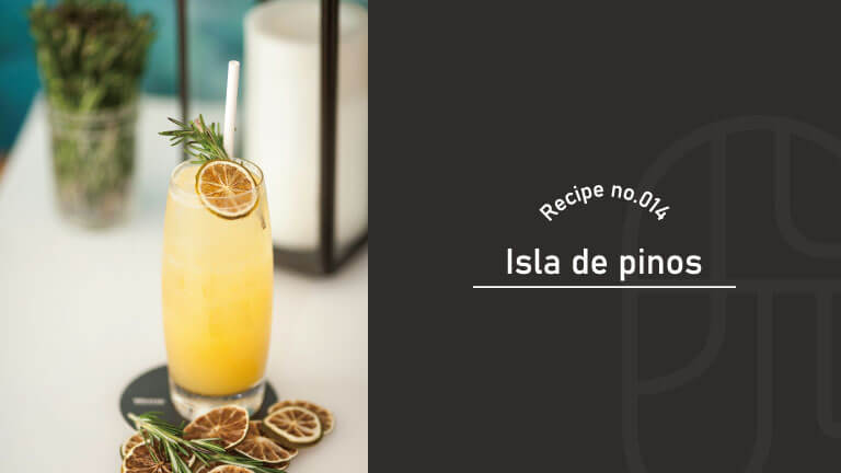 A tall glass of orange-colored Isla de Pinos cocktail garnished with rosemary and dried citrus slices, served on a coaster