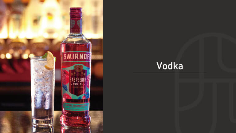 A tall glass of Smirnoff Raspberry Crush vodka cocktail with a lime wheel garnish, served next to the bottle at a bar