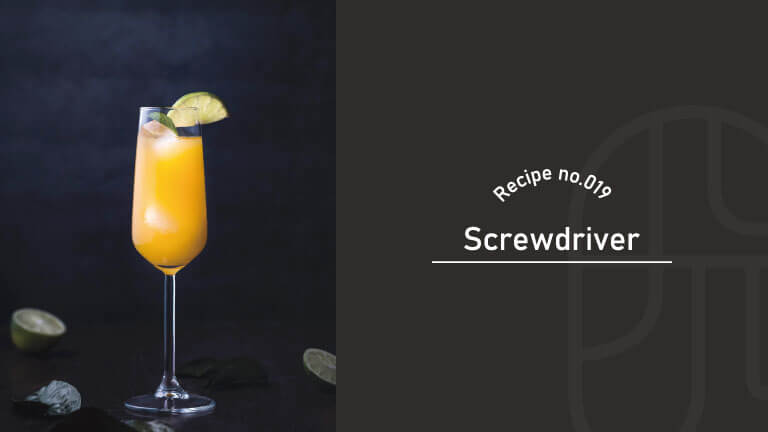 A tall flute glass filled with an orange Screwdriver cocktail, garnished with a lime wheel and served on a dark table