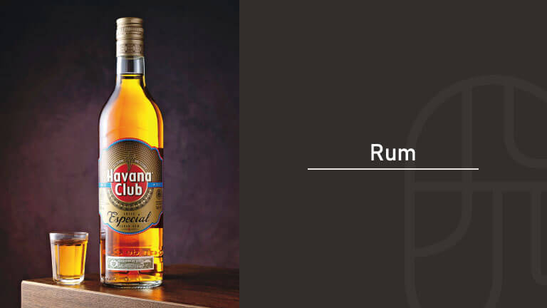 A bottle of Havana Club Especial rum beside a filled shot glass, displayed on a wooden table against a dark background