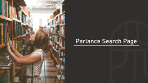 A woman browsing bookshelves in a library aisle, reaching for a book while wearing glasses