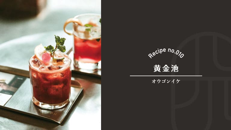 A ruby-red cocktail garnished with mint, lemon, and a cherry, served over ice in a rocks glass at a dark bar table