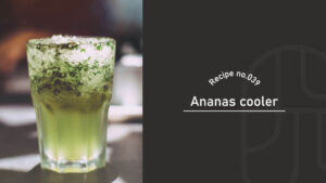 A green Ananas Cooler cocktail with crushed ice and herb garnish, served in a glass on a bar table