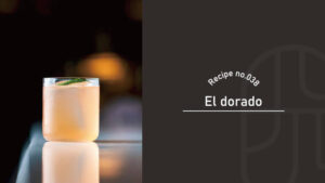 A glass of golden El Dorado cocktail garnished with mint, sitting on a reflective bar counter with warm bokeh lights