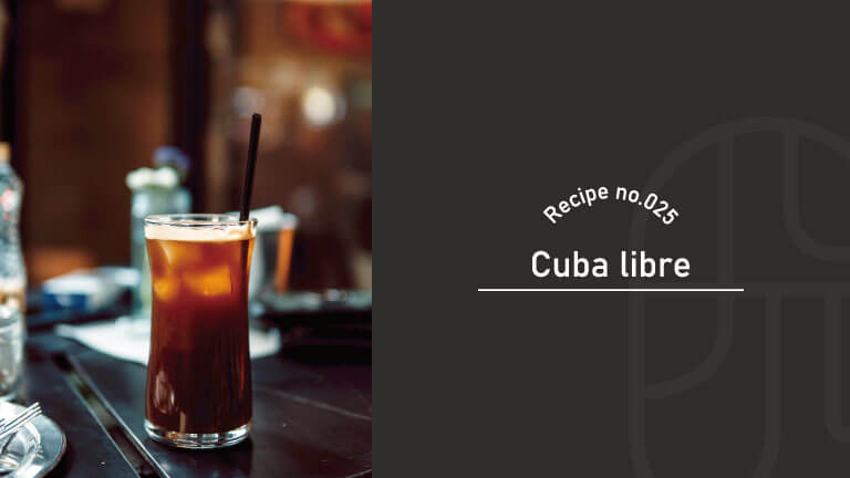 A Cuba Libre cocktail with a black straw served in a highball glass at a dimly lit bar