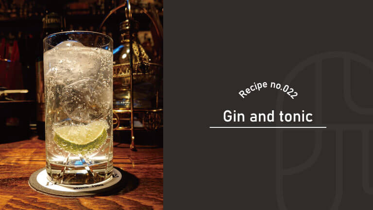 A gin and tonic garnished with a lime wheel, served in a highball glass on a wooden bar counter