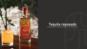 Bottle of Olmeca Reposado tequila beside a salt-rimmed orange cocktail on a wooden table, paired with a "Tequila reposado" title graphic on a dark background