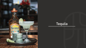 A bottle of Sierra tequila beside a salt-rimmed margarita garnished with lime, served on a wooden tray with shot glasses, paired with a "Tequila" title graphic on a dark background