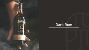A hand holding a bottle of Ron Zacapa 23 dark rum against a dark, smoky background