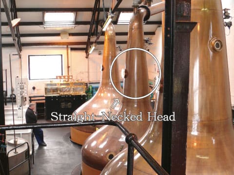 A straight-necked head on a copper pot still, highlighted with a circle, producing a heavier spirit