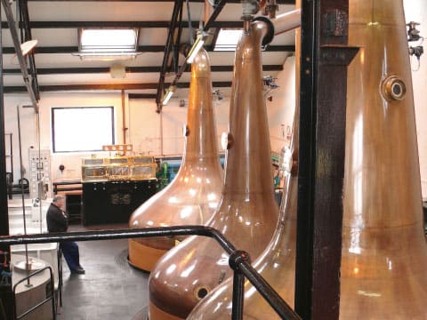 A row of tall, large copper pot stills inside a whisky distillery production hall