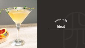 A pale golden Ideal cocktail in a coupe glass garnished with a thyme sprig, beside a grapefruit slice on a wooden coaster, next to a "Recipe no.106 Ideal" title card