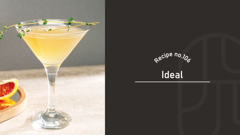 A pale golden Ideal cocktail in a coupe glass garnished with a thyme sprig, beside a grapefruit slice on a wooden coaster, next to a "Recipe no.106 Ideal" title card