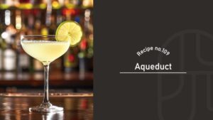 A pale yellow Aqueduct cocktail with a salted rim in a coupe glass, garnished with a lime wheel, on a bar counter with bottles in the background, beside a "Recipe no.109 Aqueduct" title card
