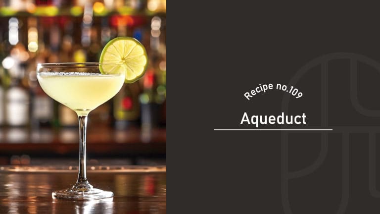 A pale yellow Aqueduct cocktail with a salted rim in a coupe glass, garnished with a lime wheel, on a bar counter with bottles in the background, beside a "Recipe no.109 Aqueduct" title card