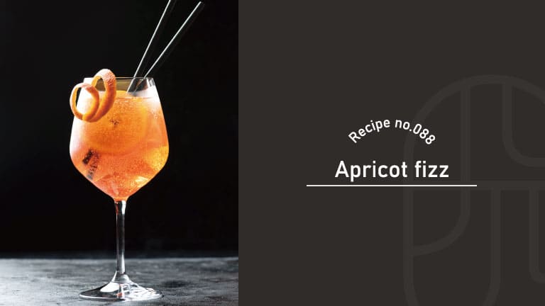 An orange Apricot Fizz cocktail served in a wine glass with an orange peel twist garnish and straws, set against a dark background