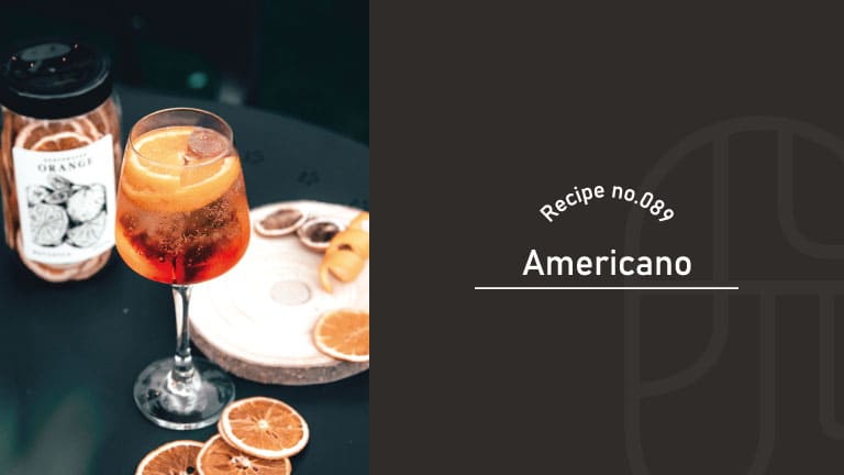 A red Americano cocktail with an orange slice garnish in a wine glass, served on a wooden board with dried citrus wheels