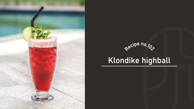 A tall glass of deep red Klondike Highball garnished with mint and a lime wheel, poolside on a stone patio, beside a "Recipe no.102 Klondike highball" title card