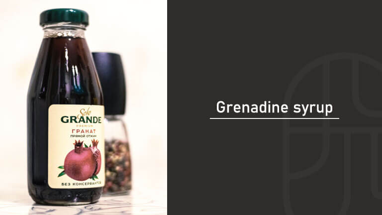 A bottle of grenadine syrup with a pomegranate label, displayed beside other bar ingredients