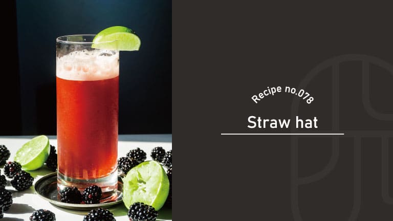 A deep red Straw Hat cocktail in a tall glass topped with foam, garnished with a lime wedge and surrounded by fresh blackberries