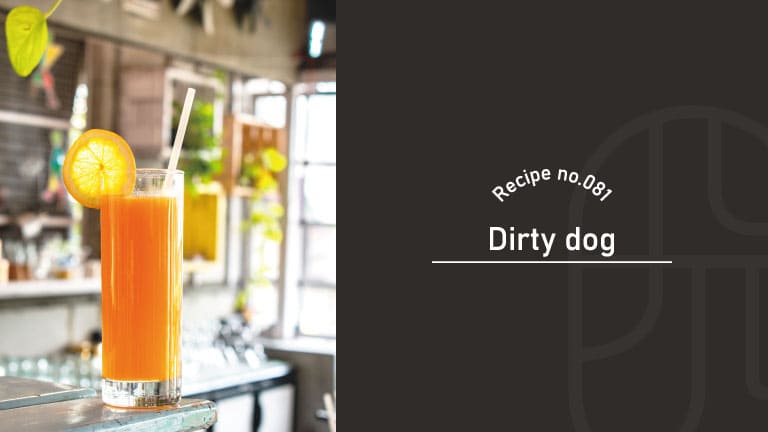 An orange Dirty Dog cocktail served in a tall glass with a straw and orange slice garnish, set in a bright cafe interior
