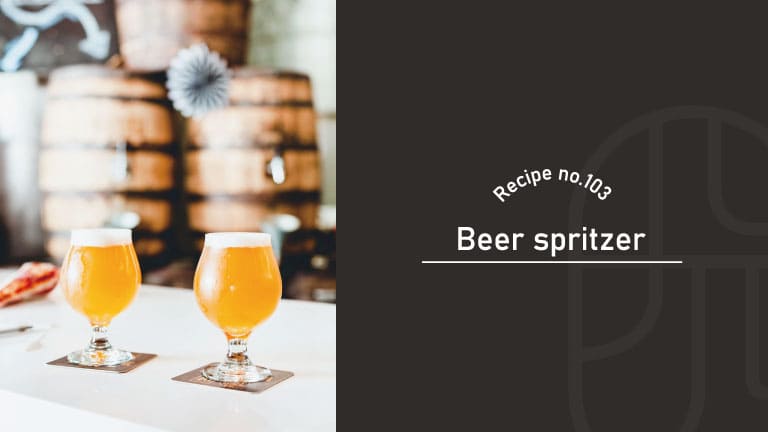 Two glasses of golden Beer Spritzer with white foam, set on coasters against blurred wooden barrels, beside a "Recipe no.103 Beer spritzer" title card