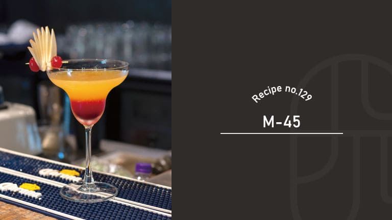 M-45 cocktail with an orange-to-red gradient in a margarita-style glass, garnished with an apple fan and red cherries on a bar mat