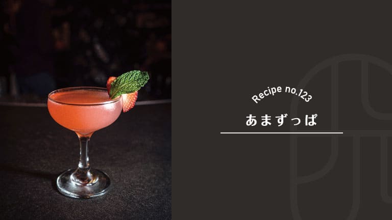 Amazuppa cocktail, a Japanese sweet-and-sour drink, with a soft pink color in a coupe glass garnished with a strawberry slice and fresh mint on a dark bar counter