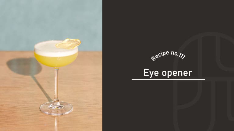 A pale yellow Eye Opener cocktail with a frothy white top in a coupe glass, garnished with a lemon twist, on a wooden table against a teal wall, beside a "Recipe no.111 Eye opener" title card