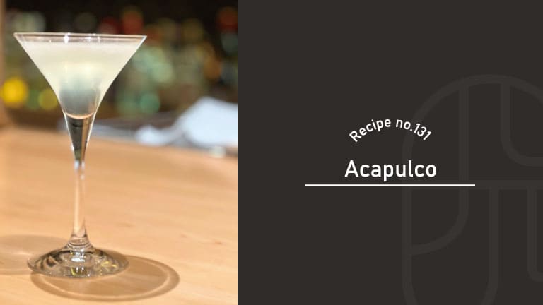 Acapulco cocktail with a pale, cloudy white color in a martini glass on a wooden bar counter, with soft bokeh lights in the background