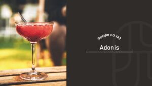 Adonis cocktail in a cut-crystal coupe glass, a deep reddish-amber drink with a thin straw, on a wooden table in a sunlit garden — Recipe no.142