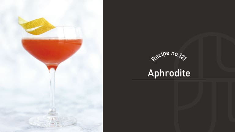 Aphrodite cocktail with a vivid coral-red color in a coupe glass, garnished with a twisted lemon peel on a white marble background