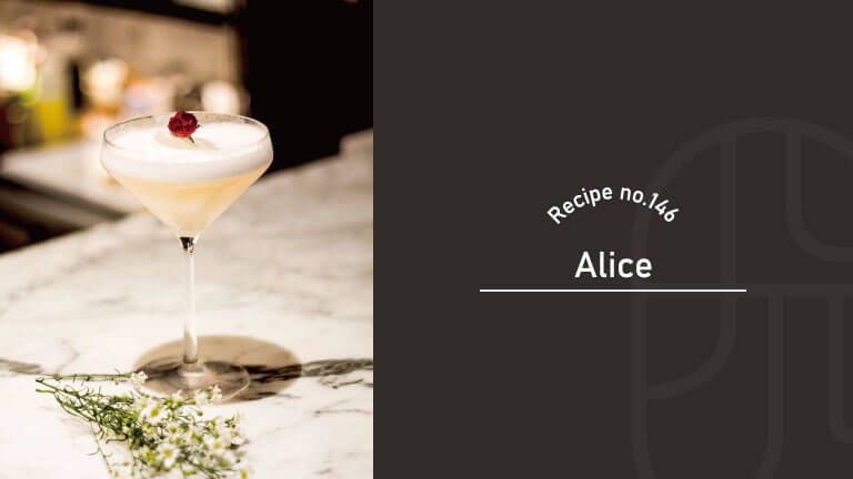 Alice cocktail in a coupe glass, a pale golden drink topped with silky white foam and a single dried rosebud, on a marble bar counter with small white wildflowers — Recipe no.146